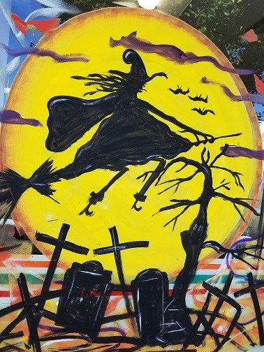 image painted on the window of a 7-11 of a witch riding a broomstick over a cemetery
